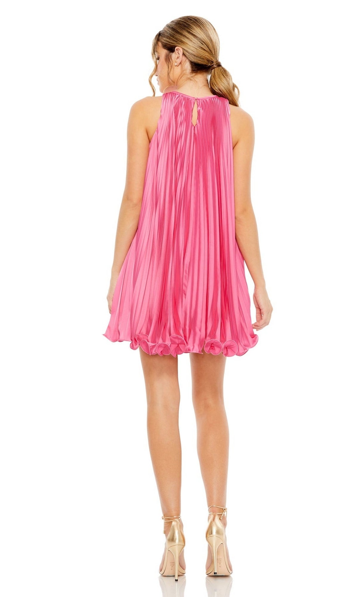 A woman faces away, wearing the Mac Duggal 49636 short pleated semi-formal dress in pink with a high neck and gold heels, her hair styled in a loose ponytail.
